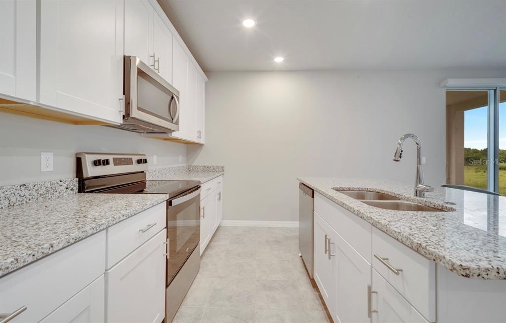 A kitchen features white cabinets, granite countertops, stainless steel appliances, and a central island — 491 WHISTLING DUCK TRAIL, ST CLOUD, FL