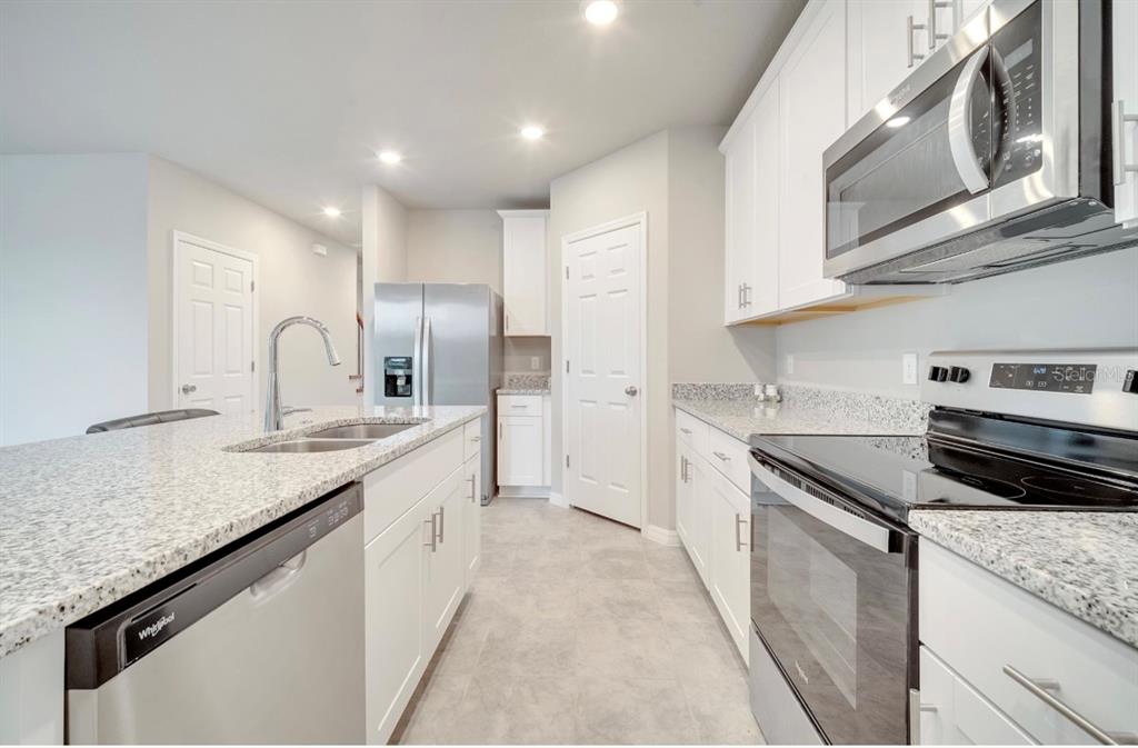 A modern kitchen features white cabinets, granite countertops, stainless steel appliances, and a central island — 491 WHISTLING DUCK TRAIL, ST CLOUD, FL