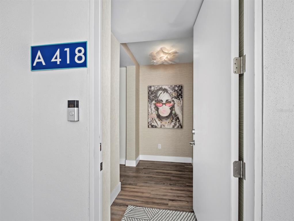 A view through an open doorway into an apartment entryway with wood-look flooring and artwork — 1709 N TAMIAMI TRAIL UNIT 418, SARASOTA, FL