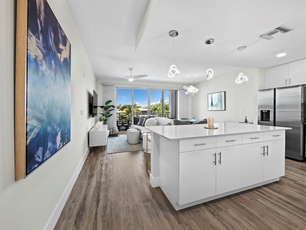 A modern open-concept kitchen and living area features white cabinetry, a central island, and balcony access — 1709 N TAMIAMI TRAIL UNIT 418, SARASOTA, FL