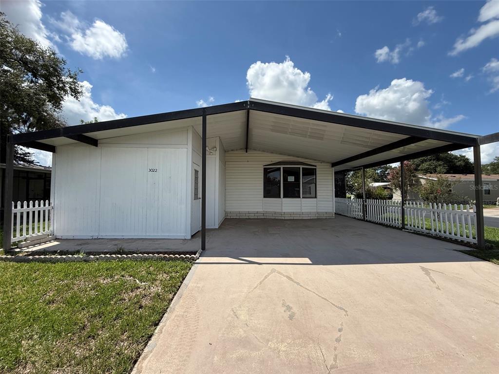 A single-story home features a large attached carport, white siding, and a white picket fence — 3022 SHORT LEAF STREET, WESLEY CHAPEL, FL