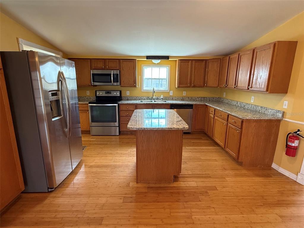 A kitchen features wood cabinets, stainless steel appliances, a granite island, and hardwood flooring — 3022 SHORT LEAF STREET, WESLEY CHAPEL, FL