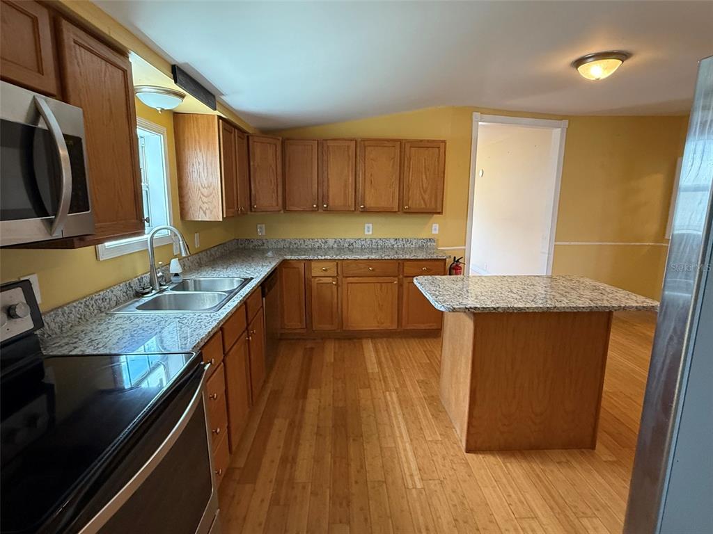 A kitchen with wood cabinets, granite countertops, a center island, and light wood flooring — 3022 SHORT LEAF STREET, WESLEY CHAPEL, FL