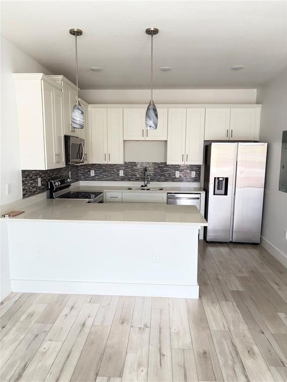 A kitchen features white cabinets, stainless steel appliances, a quartz countertop, and light wood flooring — 1619 CUMIN DRIVE, POINCIANA, FL
