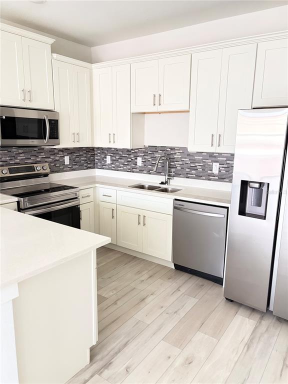 A kitchen features white cabinets, stainless steel appliances, a tiled backsplash, and light wood flooring — 1619 CUMIN DRIVE, POINCIANA, FL