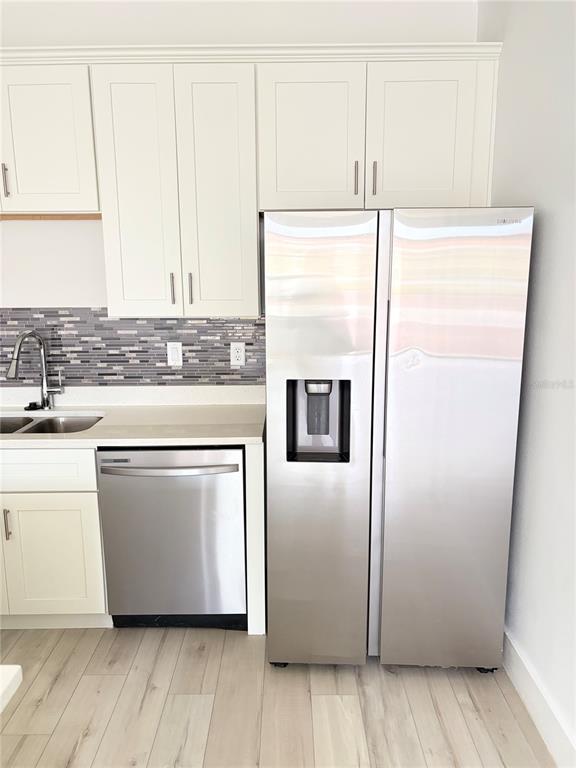A kitchen features white cabinets, stainless steel appliances, and a gray tiled backsplash — 1619 CUMIN DRIVE, POINCIANA, FL