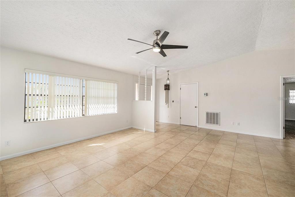 A bright, empty living room features beige tile flooring, a ceiling fan, and large windows — 909 CHIPAWAY DRIVE, APOLLO BEACH, FL