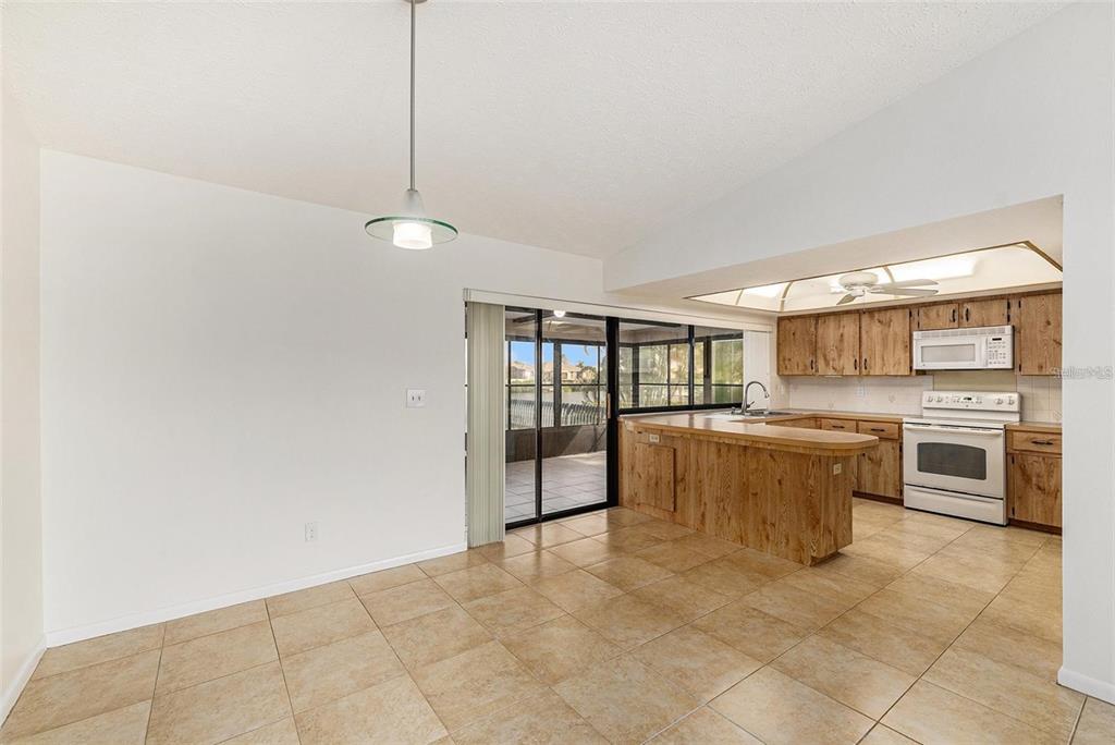 An open-concept kitchen and dining area features wood cabinets, tile flooring, and a sliding glass door — 909 CHIPAWAY DRIVE, APOLLO BEACH, FL