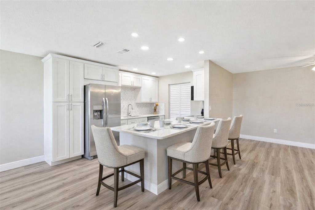 A modern kitchen features white cabinetry, a large central island with seating, and light wood flooring — 1203 16TH CIRCLE SE, LARGO, FL