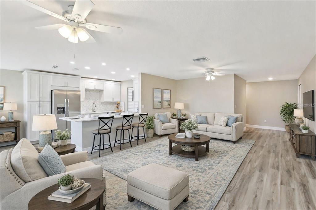 An open-concept living room and kitchen featuring light wood flooring, neutral furniture, and ceiling fans — 1203 16TH CIRCLE SE, LARGO, FL