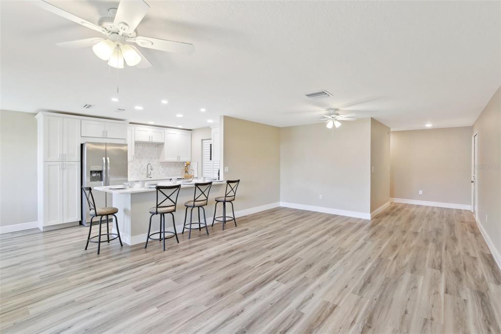 An open-concept kitchen and living area featuring white cabinetry, a breakfast bar, and wood-look flooring — 1203 16TH CIRCLE SE, LARGO, FL
