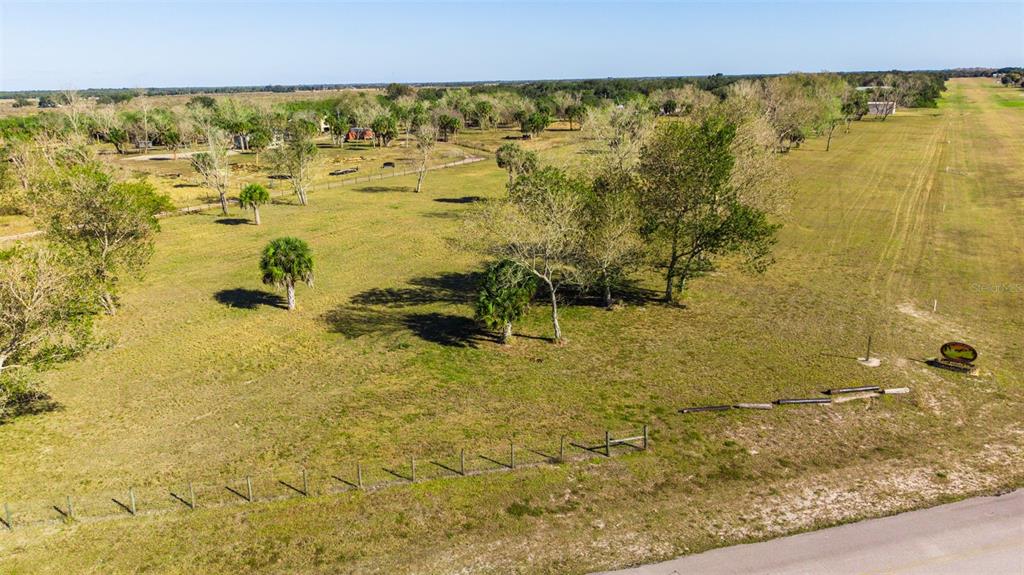 An aerial view of a large, grassy, fenced-in lot with scattered trees and a paved road — SW 144TH PARKWAY, OKEECHOBEE, FL