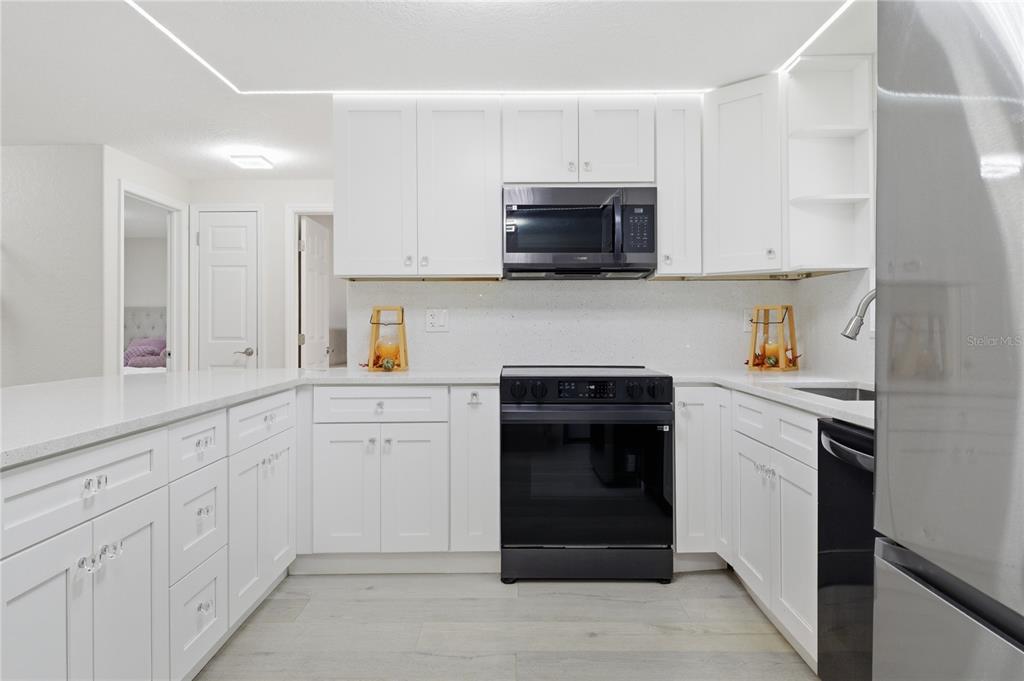 A white kitchen features black appliances, quartz countertops, and light wood-look flooring — 6338 ABERDEEN AVENUE, NEW PORT RICHEY, FL
