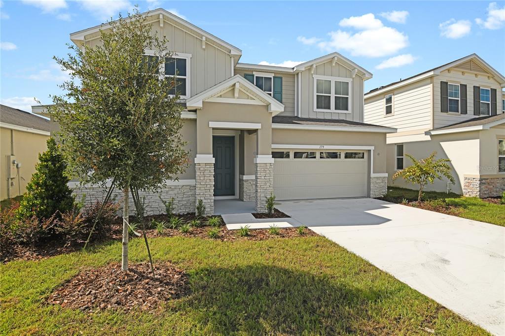 A two-story suburban house with a beige exterior, stone accents, and a two-car garage — 179 FLAG LILLY LANE, UMATILLA, FL