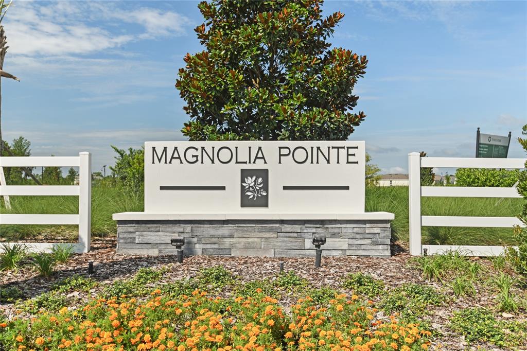 A white Magnolia Pointe community entrance sign stands behind a bed of orange flowers — 179 FLAG LILLY LANE, UMATILLA, FL
