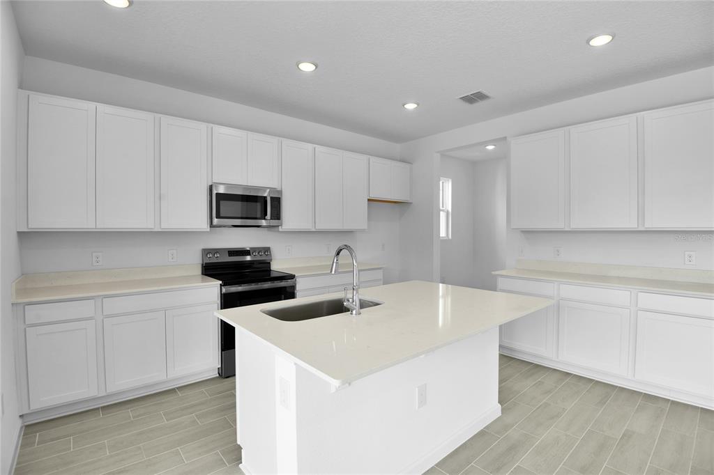 A modern kitchen features white cabinets, a central island with a sink, and stainless appliances — 179 FLAG LILLY LANE, UMATILLA, FL
