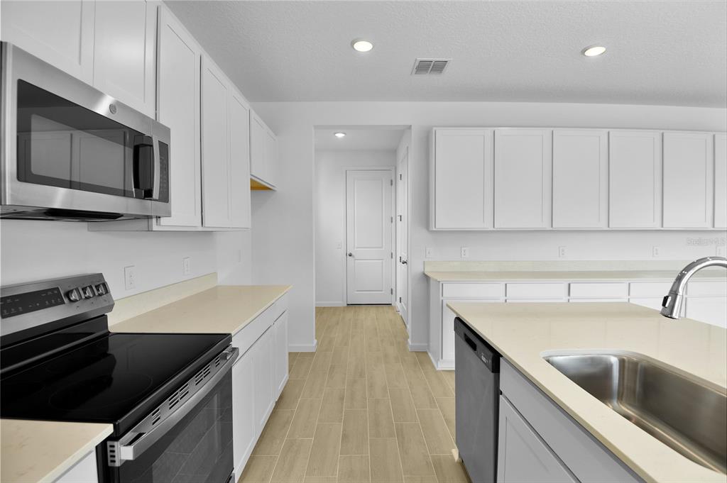 A kitchen features white cabinets, light countertops, stainless steel appliances, and wood-look tile flooring — 179 FLAG LILLY LANE, UMATILLA, FL