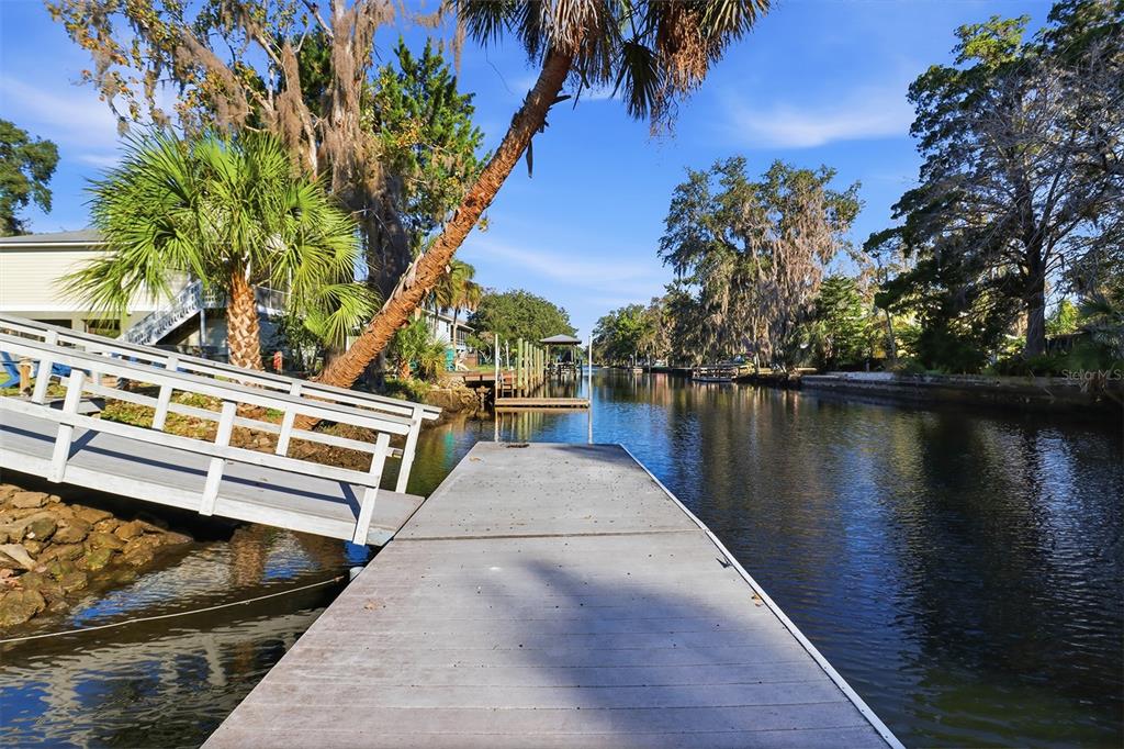 A wooden dock extends into a canal lined with trees and residential properties — 3619 N SUWANNEE POINT, CRYSTAL RIVER, FL