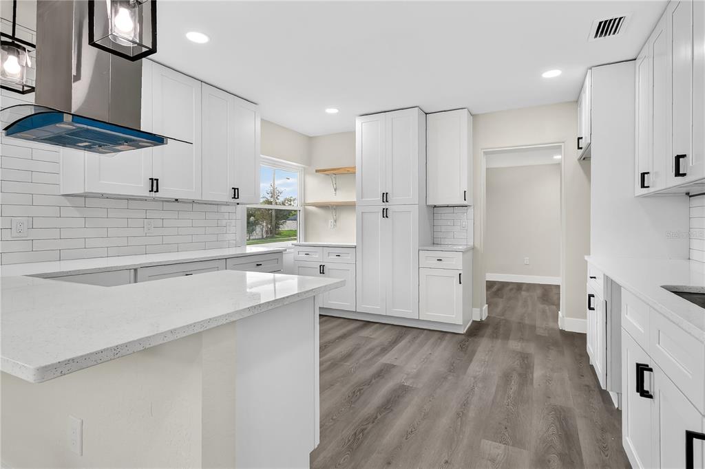 A modern kitchen features white cabinetry, quartz countertops, a subway tile backsplash, and wood-look flooring — 2612 ROXBURY ROAD, WINTER PARK, FL