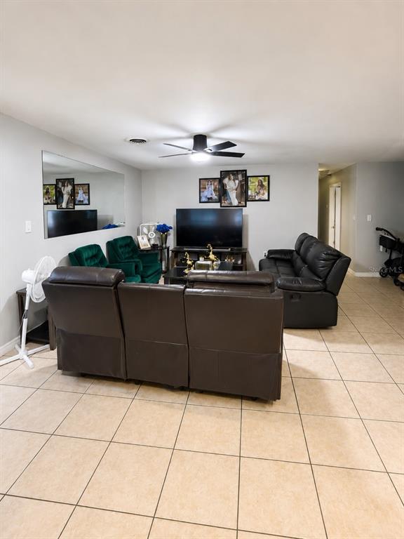 A living room features a brown leather sectional, green armchairs, a television, and tile flooring — 811 HILLSIDE AVENUE, LAKE WALES, FL