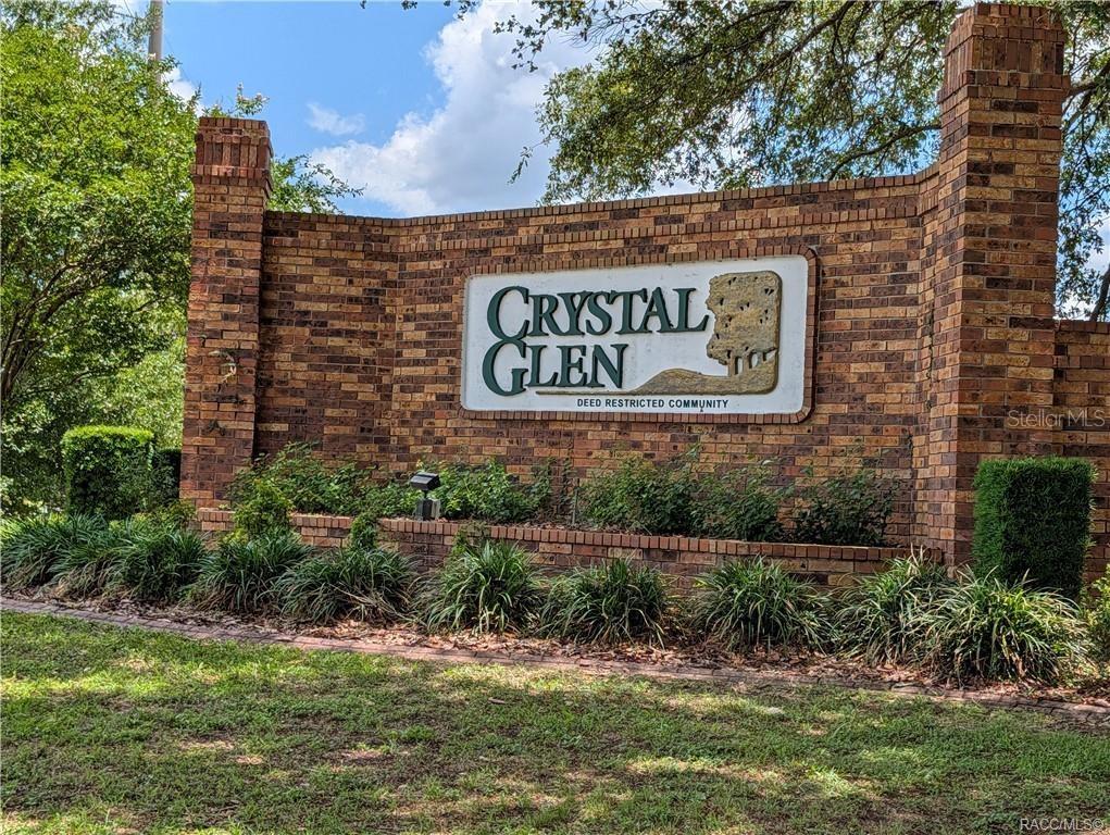 A brick entrance sign for Crystal Glen community stands in a landscaped yard — 1078 S SOFTWIND LOOP, LECANTO, FL