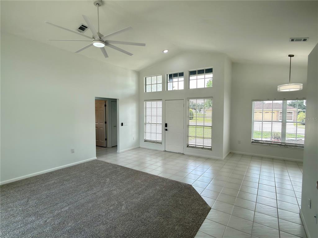 A living room with vaulted ceilings, a ceiling fan, carpeted and tiled flooring, and windows — 1078 S SOFTWIND LOOP, LECANTO, FL