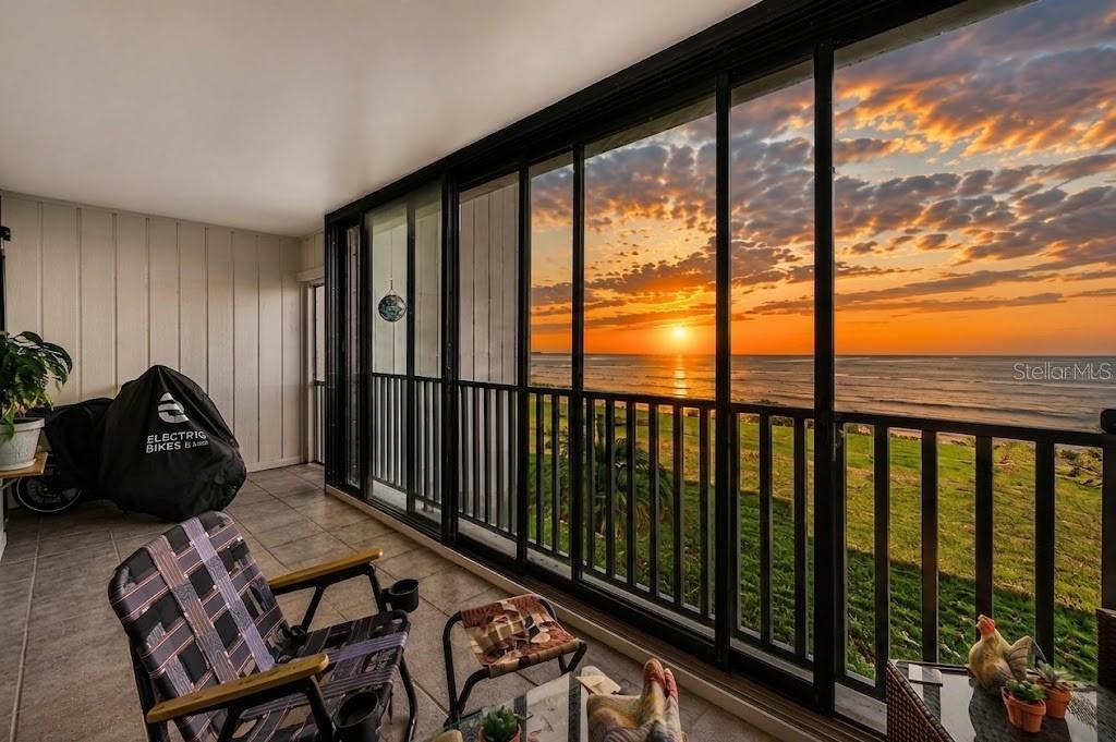 A balcony with tile flooring, patio furniture, and a covered bicycle overlooks a sunset ocean view — 828 BAHIA DEL SOL DRIVE UNIT 59, RUSKIN, FL