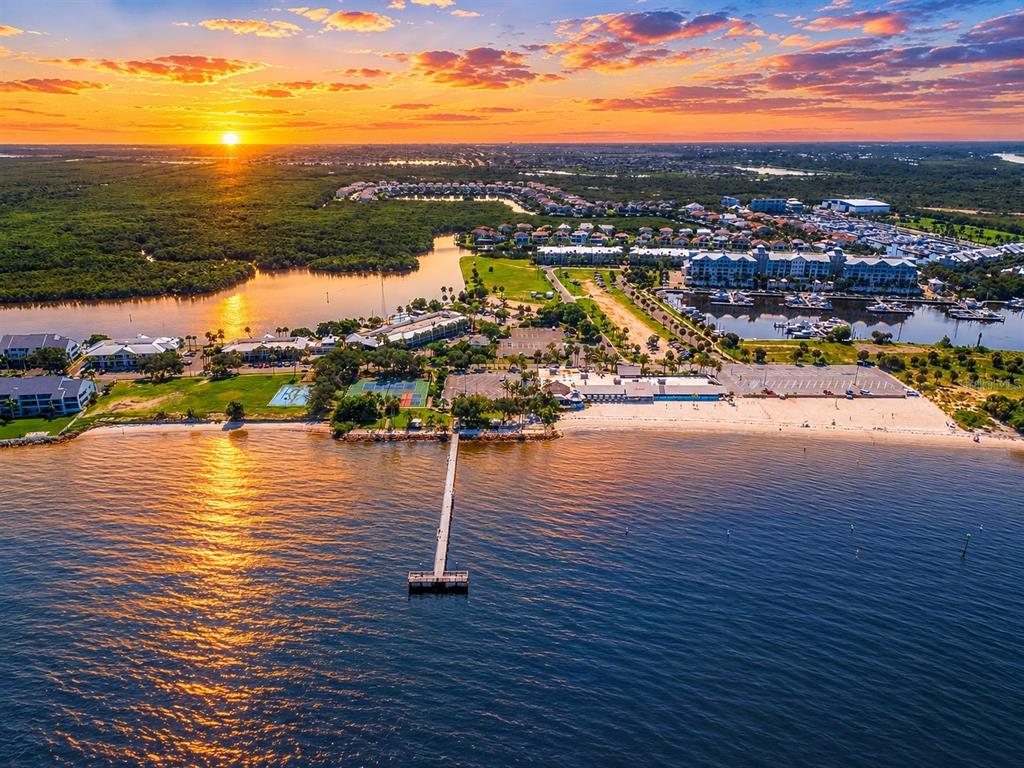 An aerial view of a coastal resort featuring a long pier, beach, and marina at sunset — 828 BAHIA DEL SOL DRIVE UNIT 59, RUSKIN, FL