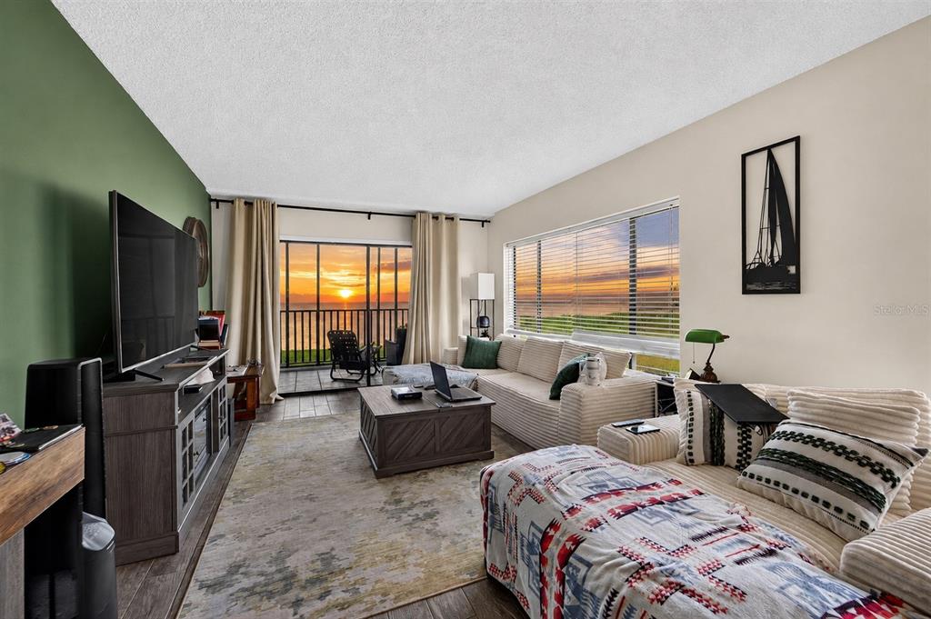 A living room with a sectional sofa, television, and a balcony overlooking a sunset view — 828 BAHIA DEL SOL DRIVE UNIT 59, RUSKIN, FL