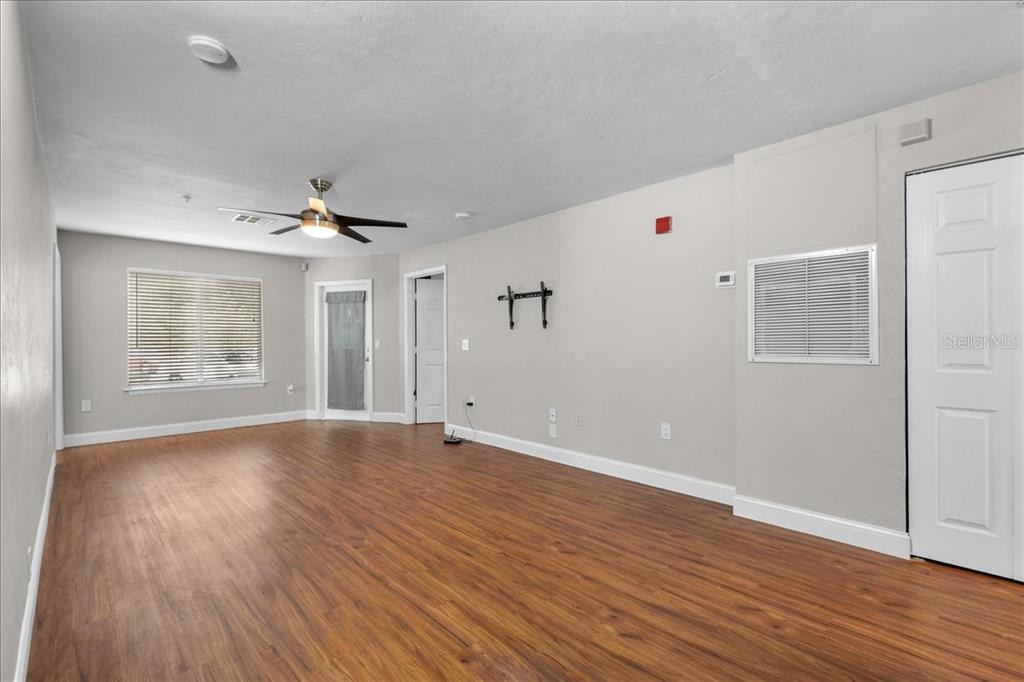 An empty room features wood-look flooring, a ceiling fan, and a white door — 4000 SW 23RD STREET UNIT 4-105, GAINESVILLE, FL