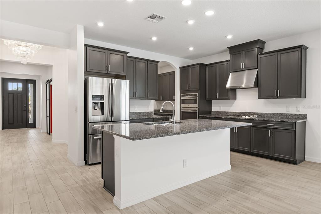 A modern kitchen features dark gray cabinetry, granite countertops, a central island, and stainless appliances — 1151 LAKESIDE ESTATES DRIVE, APOPKA, FL