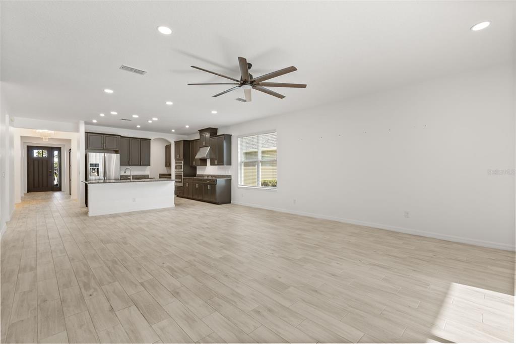 An open-concept kitchen and living area features light wood-look tile flooring and dark cabinetry — 1151 LAKESIDE ESTATES DRIVE, APOPKA, FL