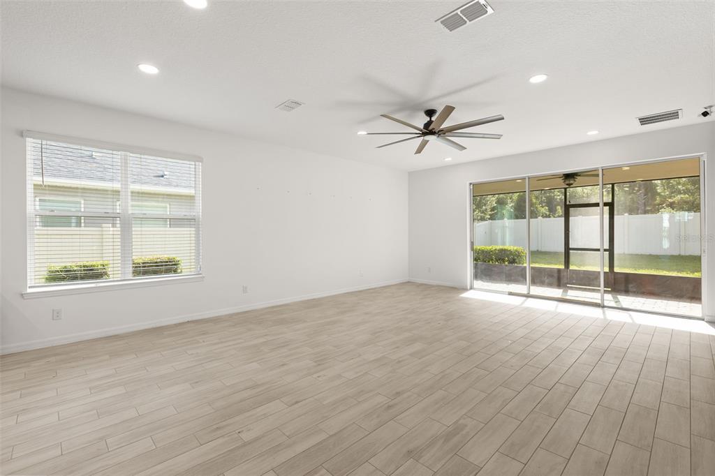 A bright, empty living room features light wood-look tile flooring, a ceiling fan, and sliding doors — 1151 LAKESIDE ESTATES DRIVE, APOPKA, FL