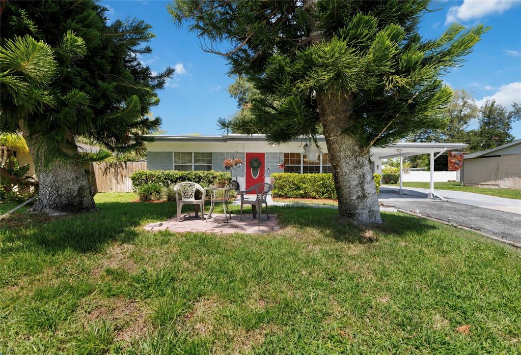 A single-story house with a red front door, a small patio, and two large pine trees — 5710 18TH STREET W, BRADENTON, FL