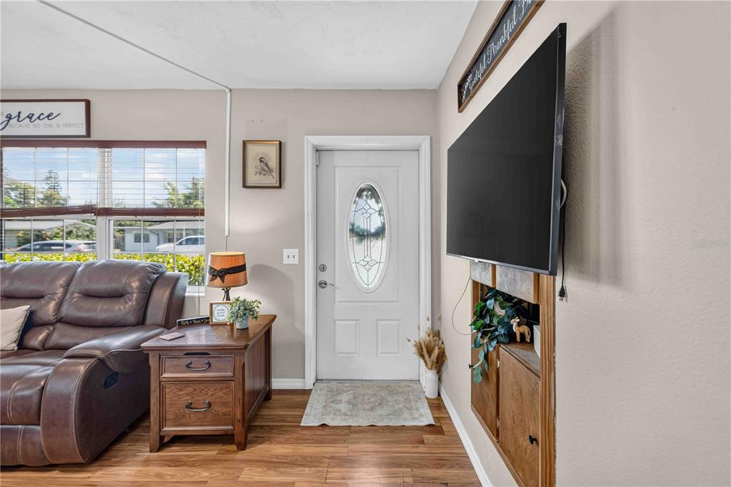 A living room features a brown leather sofa, a wooden end table, and a wall-mounted television — 5710 18TH STREET W, BRADENTON, FL