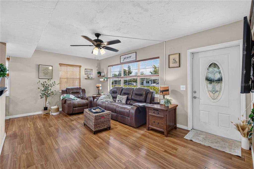 A living room featuring wood-look flooring, a brown leather sofa, a recliner, and a ceiling fan — 5710 18TH STREET W, BRADENTON, FL