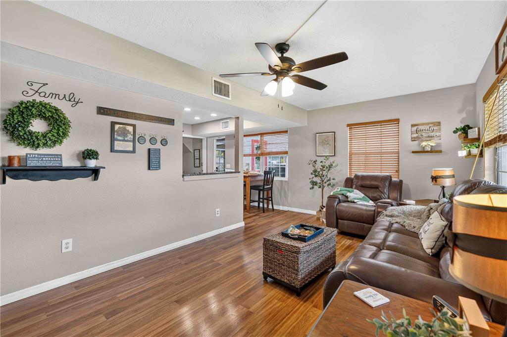 A living room with wood-look flooring, a brown leather sofa, and an open kitchen pass-through — 5710 18TH STREET W, BRADENTON, FL