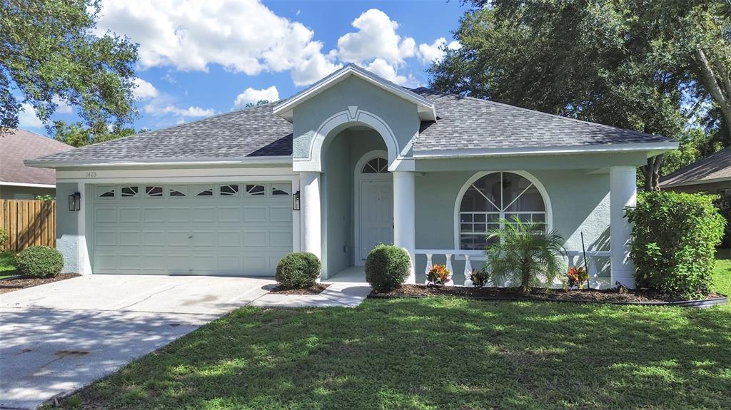 A light green single-story house with a two-car garage, arched entryway, and a front porch — 1423 LAKE SHORE RANCH DRIVE, SEFFNER, FL