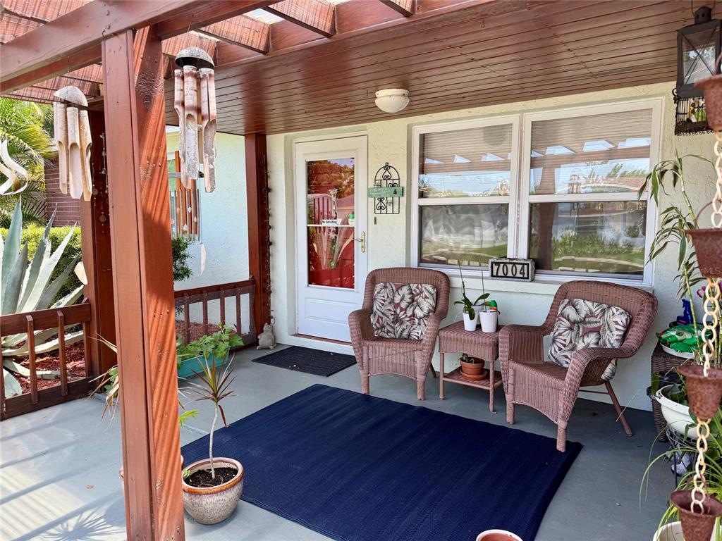 A covered front porch features two wicker chairs, a blue rug, and potted plants — 7004 ROCKWOOD DR, PORT RICHEY, FL