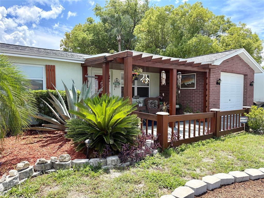 The exterior of a single-story house features a wooden pergola, brick siding, and landscaping — 7004 ROCKWOOD DR, PORT RICHEY, FL