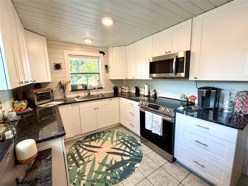 A kitchen features white cabinets, dark granite countertops, stainless steel appliances, and a patterned rug — 7004 ROCKWOOD DR, PORT RICHEY, FL