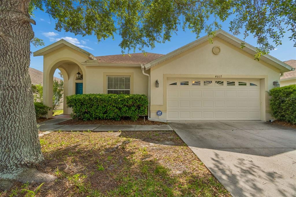 A single-story house with a beige stucco exterior, a two-car garage, and a front walkway — 4017 LANGDRUM DRIVE, WESLEY CHAPEL, FL