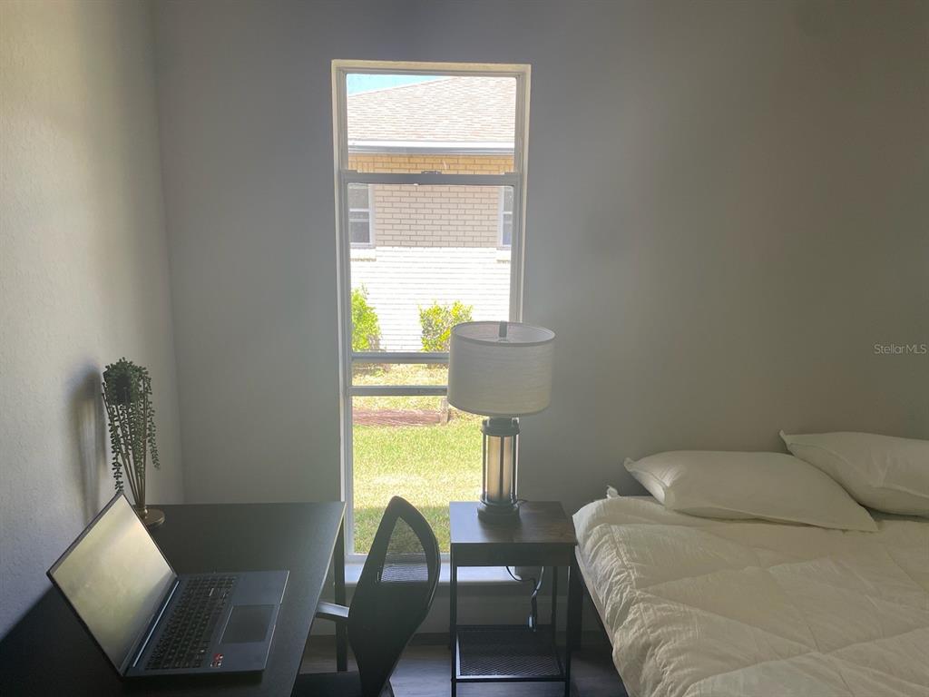 A bedroom features a desk with a laptop, a window, a nightstand, and a bed — 1216 ALAMEDA DRIVE N, LAKELAND, FL
