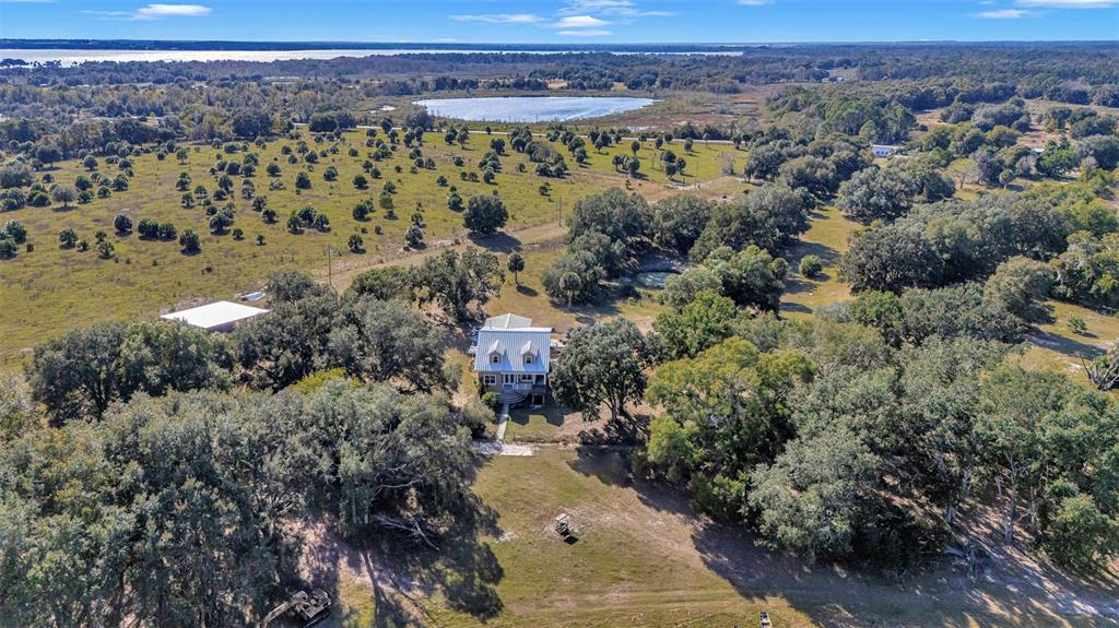 An aerial view shows a house surrounded by trees, fields, and a distant lake — 13800 COUNTY ROAD 450, UMATILLA, FL