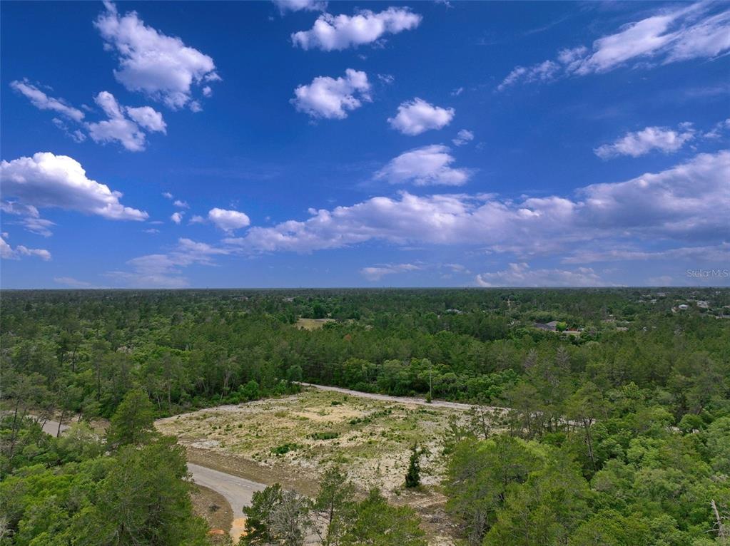 An aerial view shows a cleared, vacant lot surrounded by dense forest under a blue sky — SW 35TH TERRACE, OCALA, FL