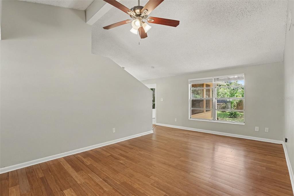 An empty living room with light gray walls, wood flooring, and a vaulted ceiling — 603 HIGHVIEW TERRACE N, BRANDON, FL