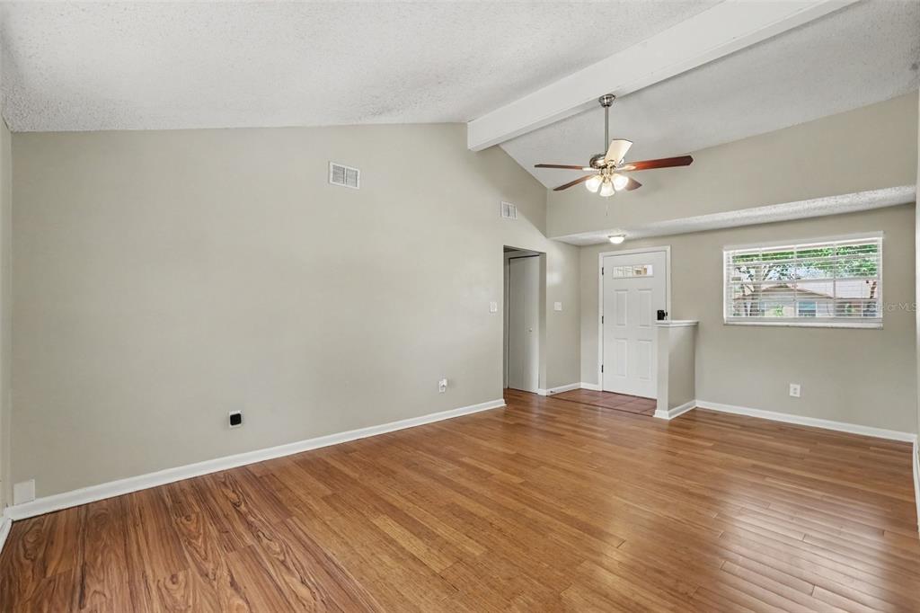 An empty living room with vaulted ceilings, wood-look flooring, a ceiling fan, and front door — 603 HIGHVIEW TERRACE N, BRANDON, FL
