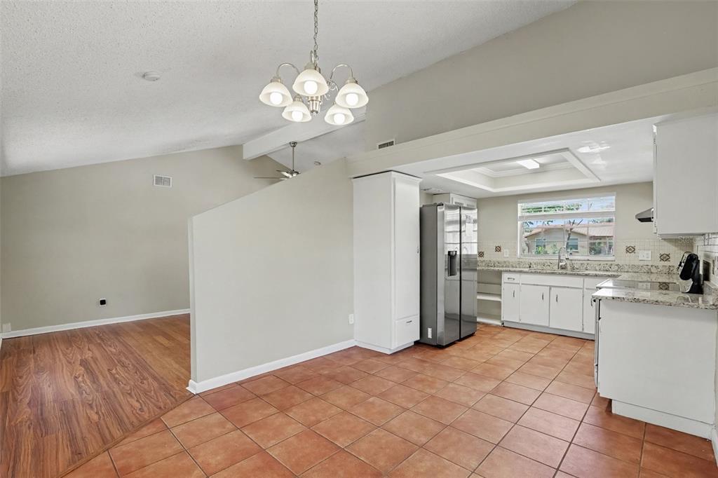 A kitchen with tile floors and white cabinets sits adjacent to a living area with wood-look flooring — 603 HIGHVIEW TERRACE N, BRANDON, FL