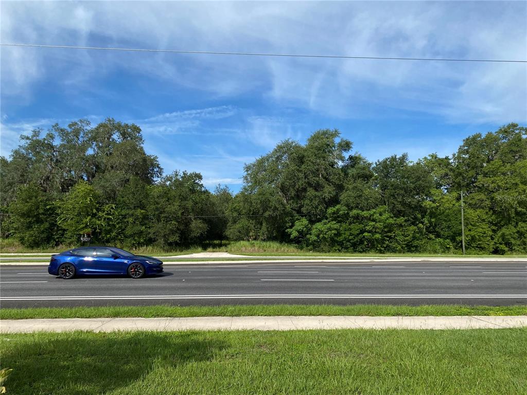 A blue car drives past a vacant, tree-lined lot along a multi-lane road — 524 S HIGHWAY 27/441, LADY LAKE, FL