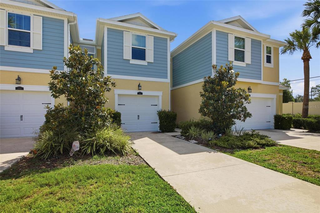 A row of attached townhomes with blue siding, yellow stucco, and white garage doors — 2013 SUNSET WIND LOOP, OLDSMAR, FL